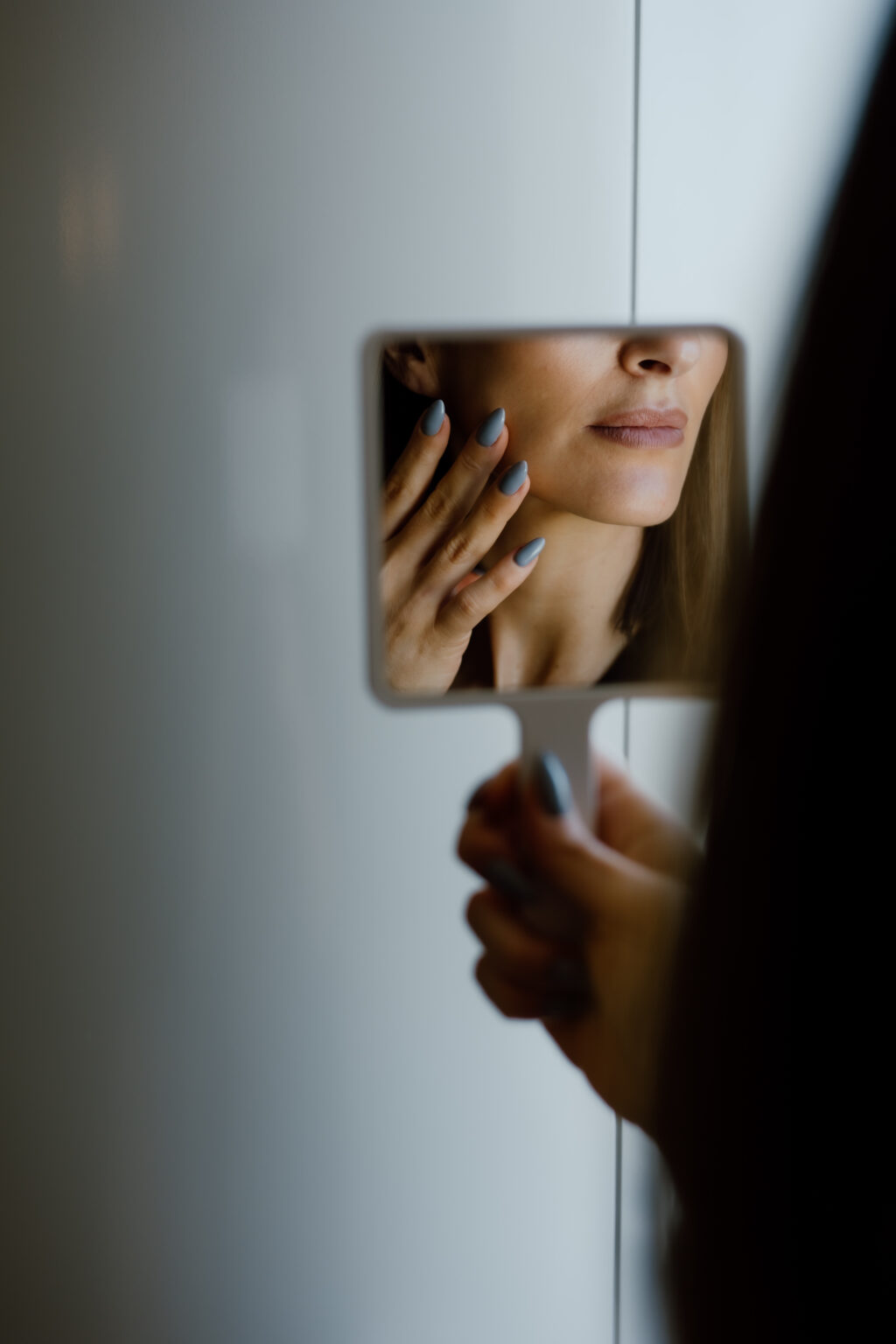 Close-up of a woman's lips and blue-gray nails visible in a small handheld mirror reflection.