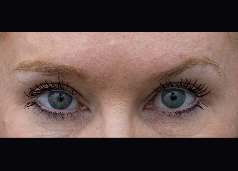 Close-up of a person’s blue eyes with curled lashes, looking straight ahead, mascara visible.