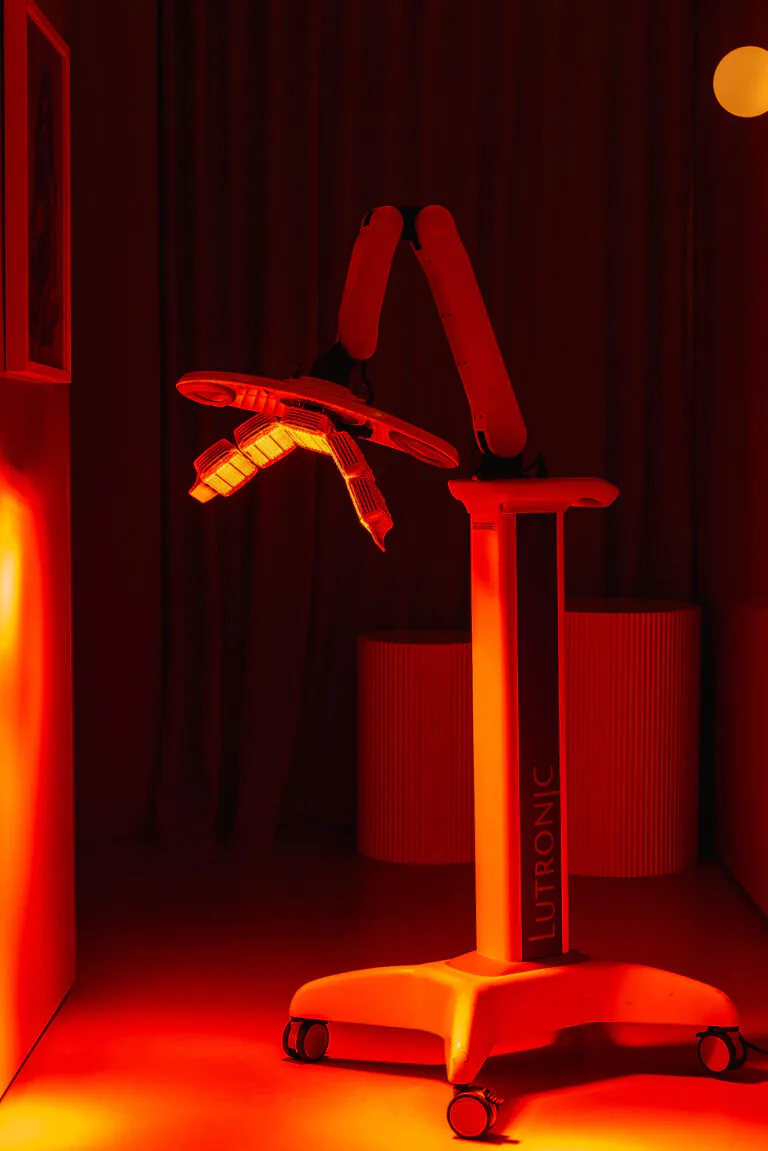 Red-lit room with a mobile robotic arm on a stand, its articulated joints glowing with red light (LUTRONIC branding).