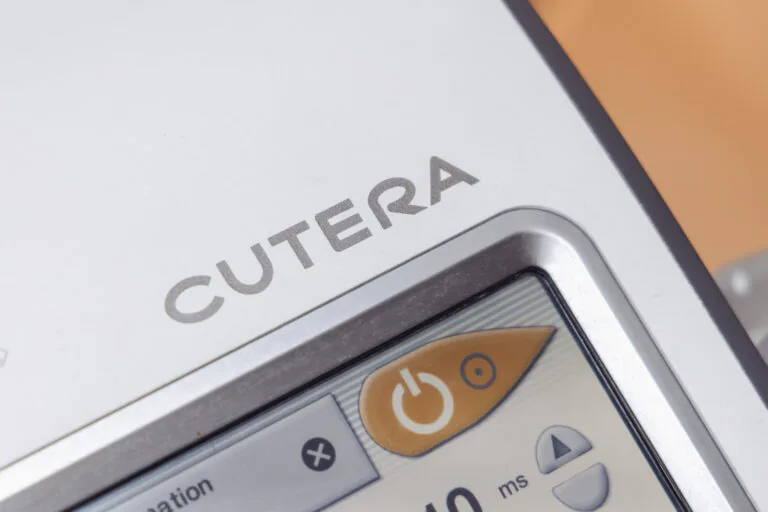 Close-up of a device control panel with an orange circular button and a grey display on a white surface.