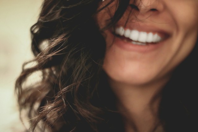 Close-up of a smiling woman’s mouth with visible white teeth and dark wavy hair framing her face.